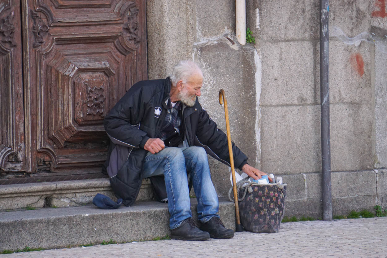 Alter Mann sitzt auf einer Treppe und wühlt im Abfall
