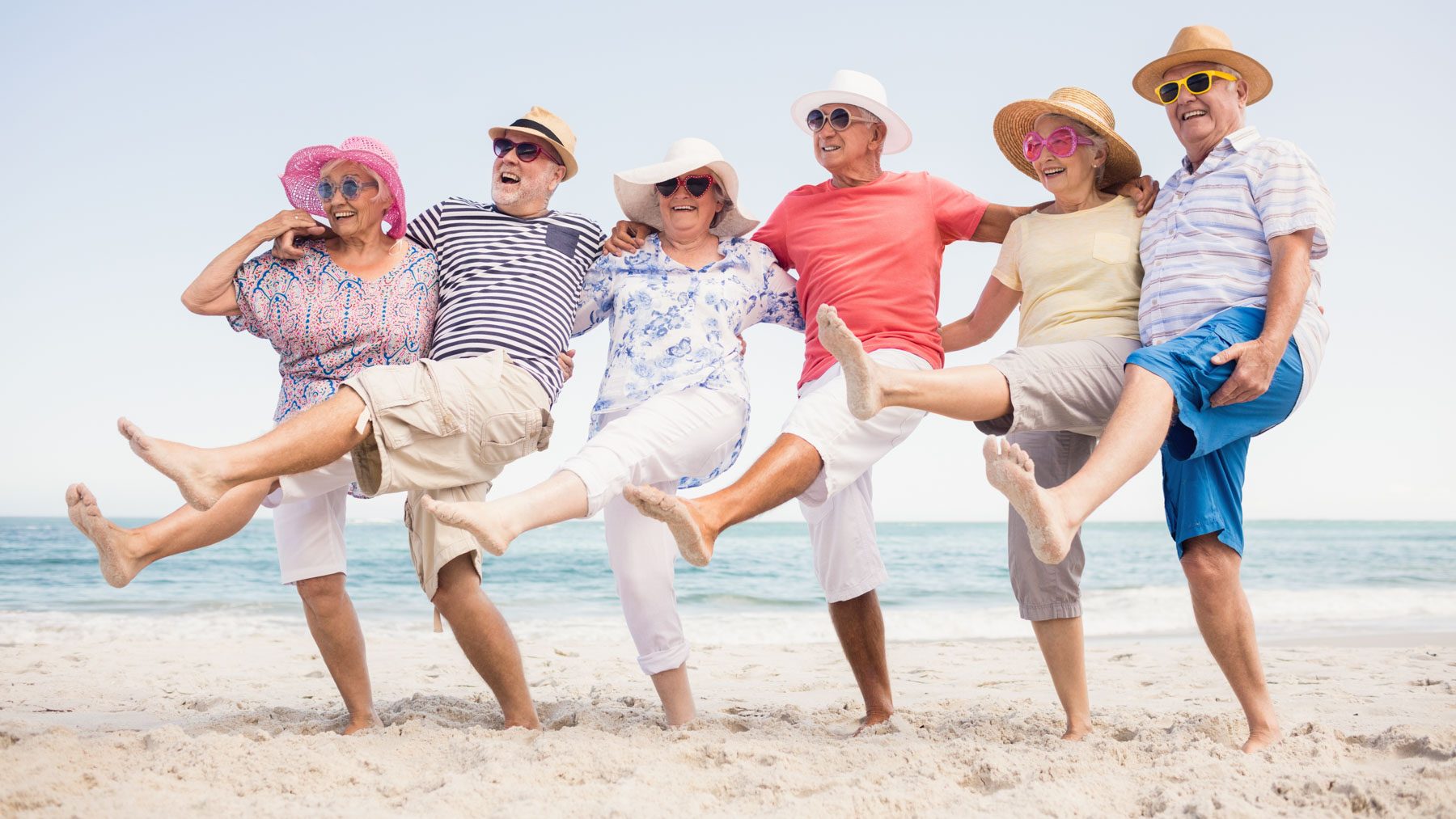 Alte Menschen tanzen am Strand und lachen.